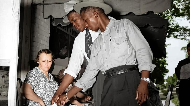 Two men in hats place slips of paper into a wooden box as a woman looks on.