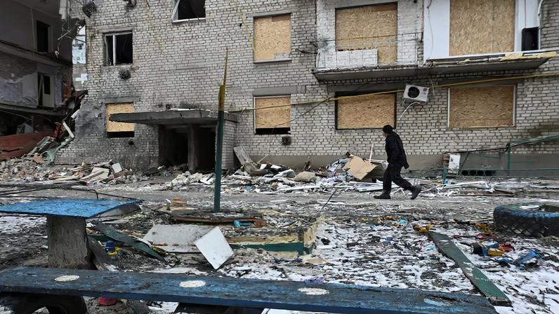 Resident walks next to an apartment building damaged by Russian military strikes in the frontline town of Komyshuvakha