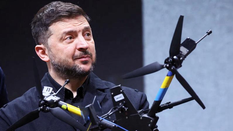 Ukrainian President Volodymyr Zelenskiy reacts as he is pictured behind a drone during his visit to a facility of German drone maker Quantum Systems, on the sidelines of the annual Munich Security Conference (MSC), near Munich, Germany, February 13, 2026.