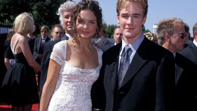 Katie Holmes in a white gown and James Van Der Beek in a dark suit pose on a red carpet.