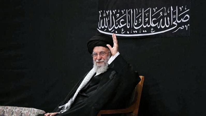 Khamenei waves while seated in a chair.