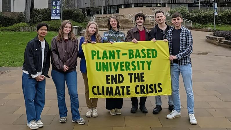 Plant-Based Universities Southampton Students stood outside the University of Southampton holding a yellow green and black banner which reads: "Plant-Based University End the Climate Crisis".