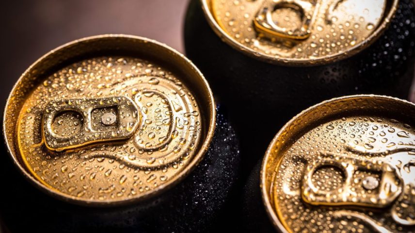 Três latas de bebida geladas com tampas douradas e gotas de condensação.