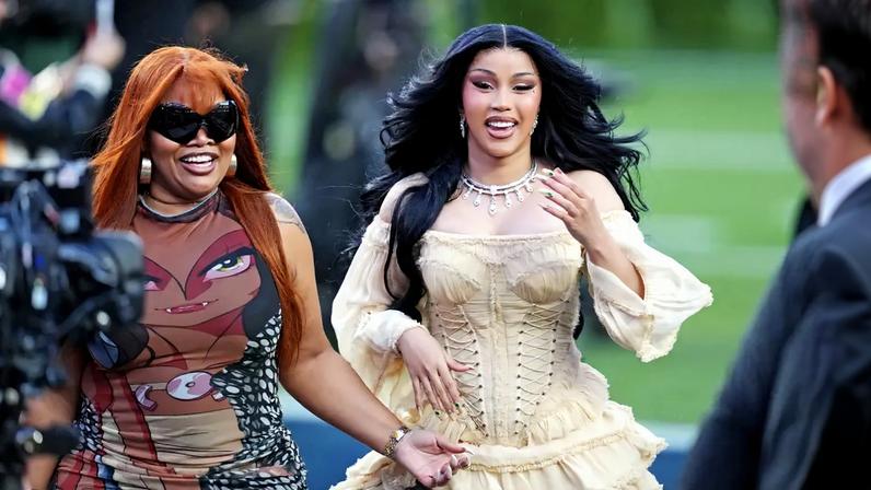 Cardi B in a cream-colored dress with ruffles and a companion in a printed top at the Super Bowl LX halftime show.