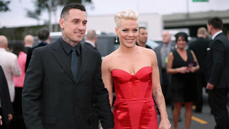Carey Hart and Pink hold hands on a red carpet.
