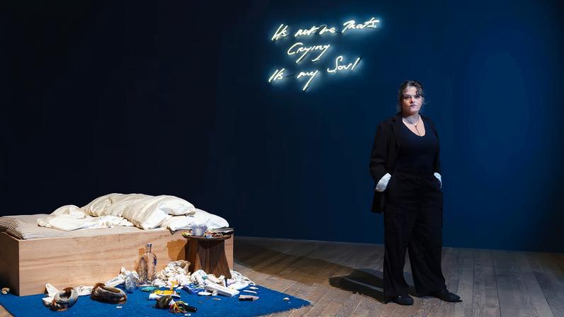 Tracey Emin standing next to My Bed, installed at her Tate Modern exhibition Second Life