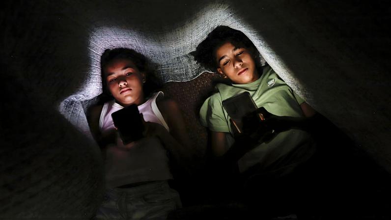 Os irmãos Clara Santana (10) e Pedro Santana (13), são vistos com celular na mão embaixo de um cobertor. Uma a cada 3 crianças tem perfil aberto em redes, alerta pesquisa Dados foram divulgados nesta terça pela Unico e Instituto Locomotiva Foto: Joédson Alves/Agência Brasil