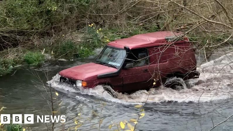 A red 4x4 drives along a section of a Hampshire chalk stream open to traffic