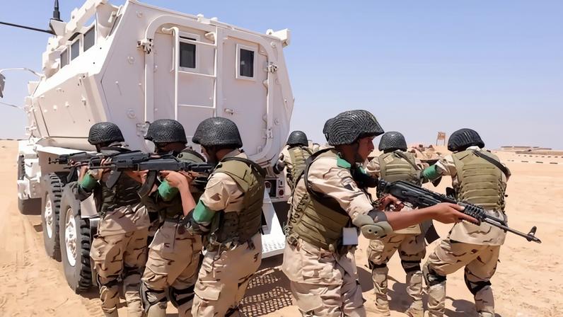 Soldiers hold guns as they stand behind an armored vehicle.