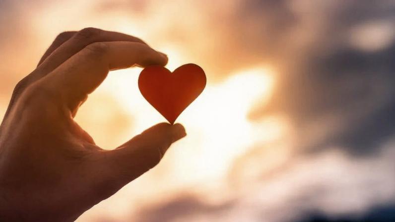 A person holds a red heart in front of a sunset. A random act of kindness can make someone’s day.