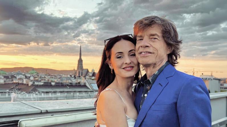 Mick Jagger and Melanie Hamrick embrace on a rooftop overlooking a city at sunset.