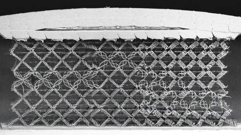 A black and white image of a woven metamaterial, comprised mostly of diamond-shaped cells woven from spiral fibers