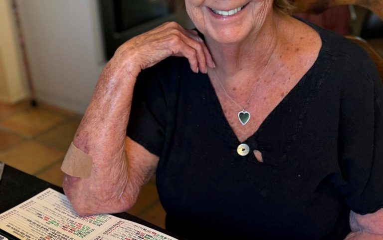 Nancy Guthrie, mother of "Today" show anchor Savannah Guthrie, smiling while sitting at a table with mahjong tiles and a card.
