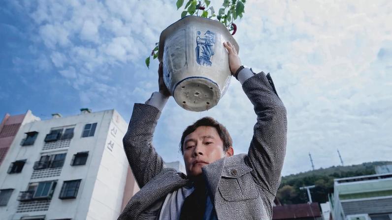 A man holds a potted plant above his head and looks down.