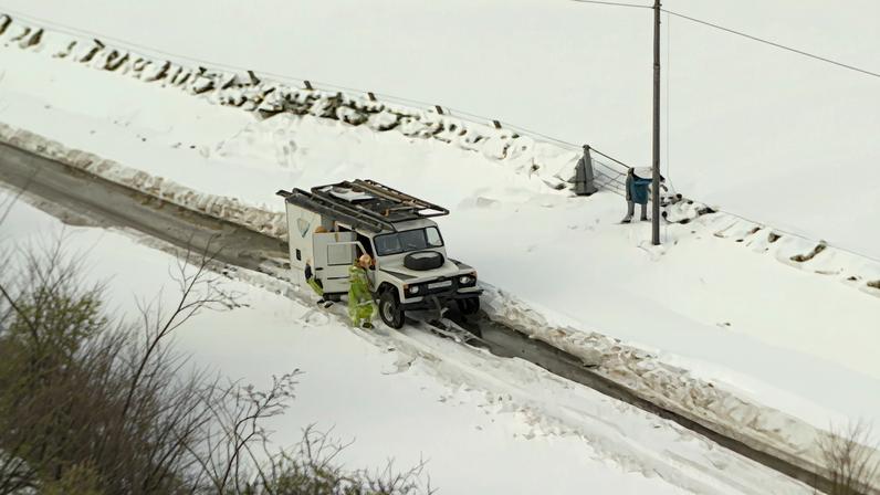 Aerial shot of a white Land Rover on a country road, surrounded by deep snow.