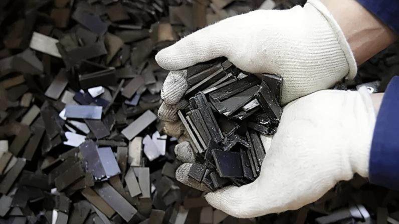 Getty Images A worker in white gloves holds a handful of shiny grey shards of magnet for recycling (Credit: Getty Images)