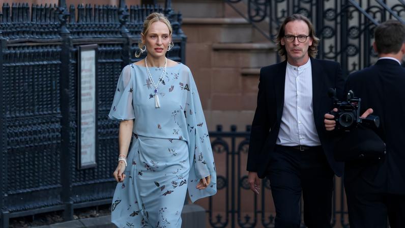 Uma Thurman in a light blue floral dress, walking on the street.