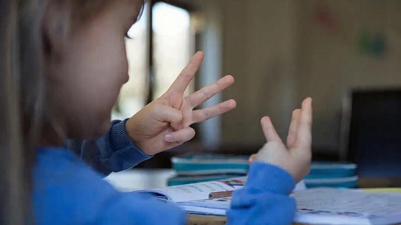 Fotografia de uma criança contando com os dedos enquanto faz a lição de casa de matemática.