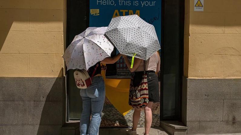 Two woman at an ATM protect themselves from the sun with umbrellas during a heatwave in Madrid, Spain, Sunday, Aug. 15, 2021.
