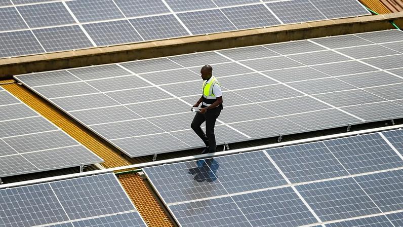 FILE - Mark Munyua, CP solar's technician, examines solar panels on the roof of a company in Nairobi, Kenya, Sept. 1, 2023.