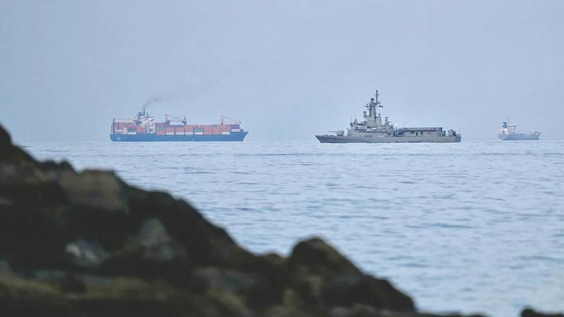 A UAE navy ship sails next to a cargo ship in the Strait of Hormuz as seen from Khor Fakkan, United Arab Emirates, Wednesday, March 11, 2026.