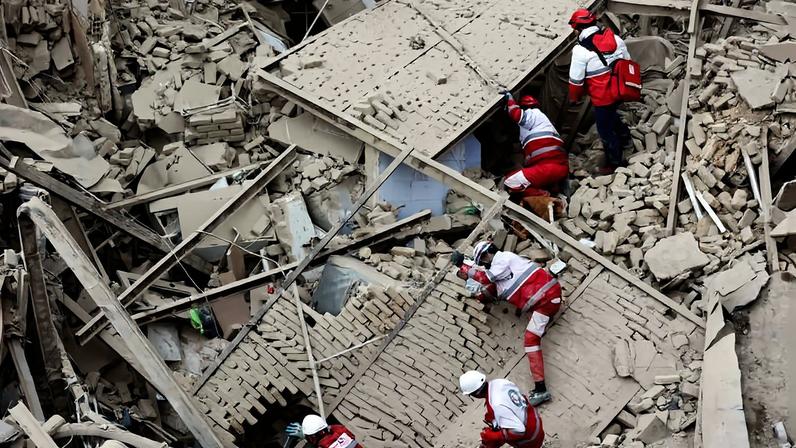 Cinco socorristas com uniformes vermelhos e capacetes brancos e vermelhos escalam e vasculham escombros de um prédio destruído. Restos de paredes, vigas e destroços de concreto estão espalhados pelo local.