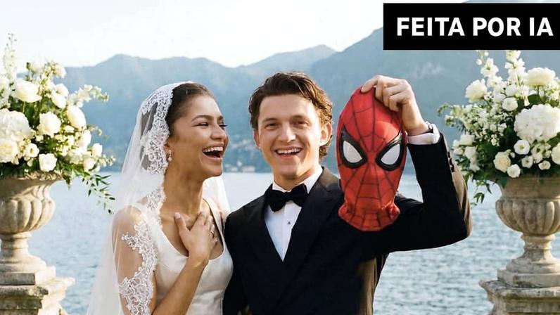 Noivos posam sorrindo em cerimônia ao ar livre com lago e montanhas ao fundo. Noivo veste terno preto e segura máscara do Homem-Aranha, noiva usa vestido branco com véu rendado. Arranjos florais brancos decoram escadaria de pedra.