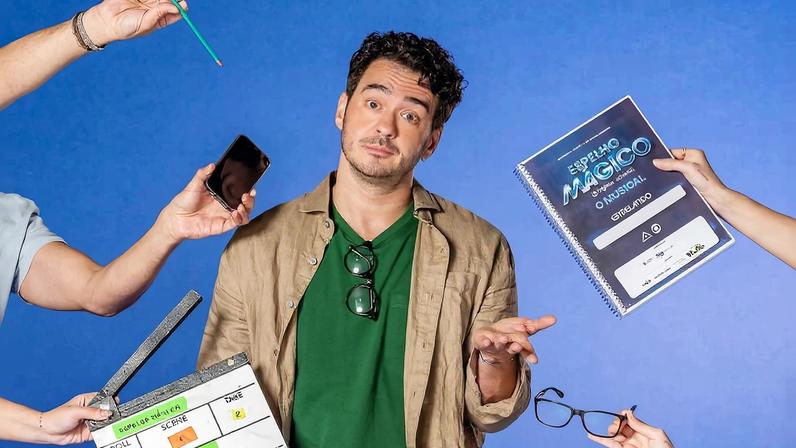 Homem de cabelo curto e escuro, vestindo camiseta verde e jaqueta bege, está no centro com expressão de dúvida. Ao redor, quatro mãos seguram objetos relacionados a filmagem: um clapperboard, um celular, um certificado e um par de óculos. Fundo azul liso.