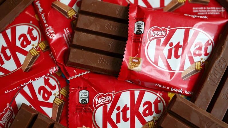 Barras de chocolate Kit Kat: algumas em embalagens vermelhas, uma aberta, e outras desembrulhadas.