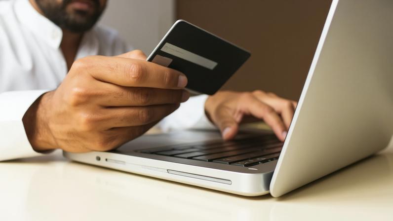 Pessoa segura cartão em frente a computador. E-commerce, venda online