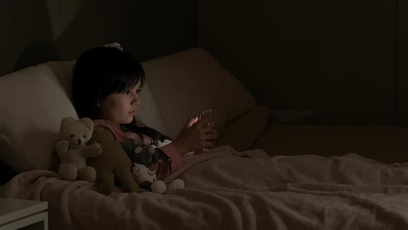 Fotografia de uma criança deitada mexendo no celular.