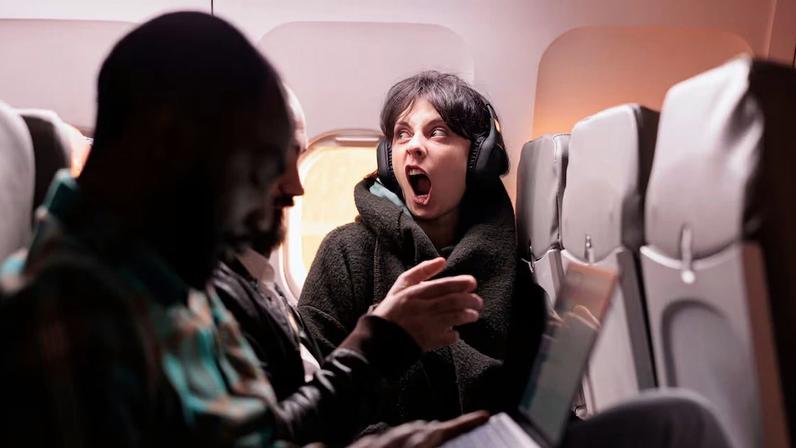 Multiethnic group of people flying abroad in economy class, using laptop, smartphone and headphones during sunset flight. Passengers travelling with international commercial airline.