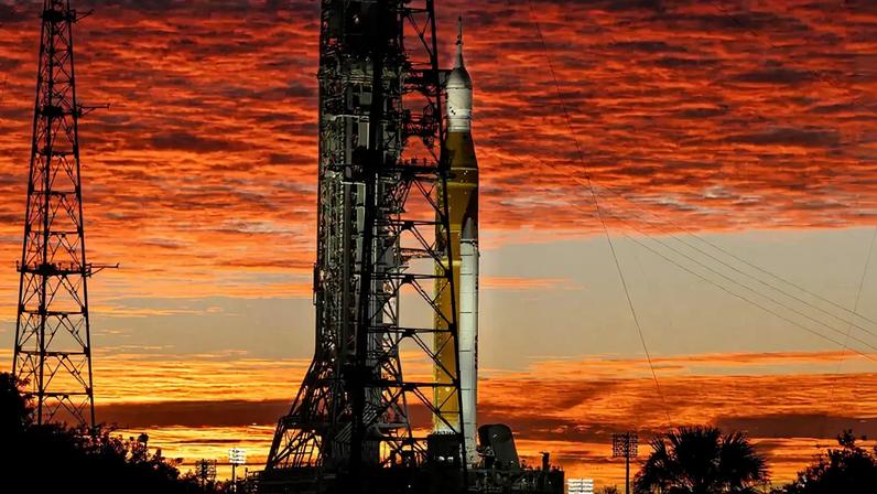 Fotografia de Nuvens e o Sol iluminam o céu na quarta-feira, 28 de janeiro de 2026, enquanto o foguete Artemis II SLS (Space Launch System) da NASA e a espaçonave Orion permanecem na vertical no Complexo de Lançamento 39B do Centro Espacial Kennedy, na Flórida.