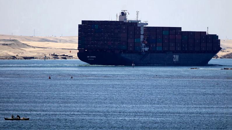 A fisherman travels on a boat with his family in front of the Zim Europa container ship, in the Suez canal