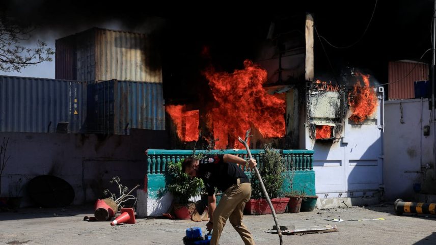 Un agente de policía recupera objetos frente a un puesto de control policial incendiado por manifestantes cerca del Consulado General de Estados Unidos en Karachi, Pakistán, este domingo.