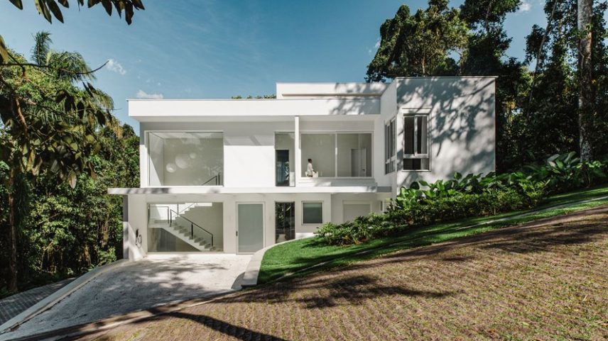 FACHADA | A arquitetura modernista original da casa foi mantida, com algumas intervenções, como a criação de grandes aberturas que ampliam a entrada de luz natural e aproximam os interiores do entorno natural. A fachada ganhou textura branca StoTex, da Sto. Na entrada, plantas criam volume, como maranta-charuto, 'Philodendro melinonii' e 'Philodendro danteanum', com paisagismo assinado por Helena Elias. Engenharia da Tecsa