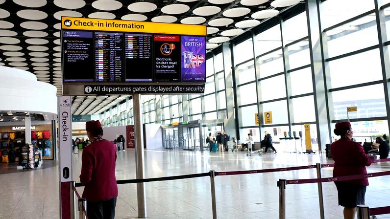 Qatar airline staff stand by a departure board displaying cancelled flights to Middle East countries amid the U.S.-Israel conflict with Iran, at Heathrow Airport