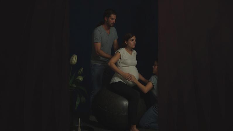 Pregnant woman sitting on a birthing ball while two caregivers support her during labor.