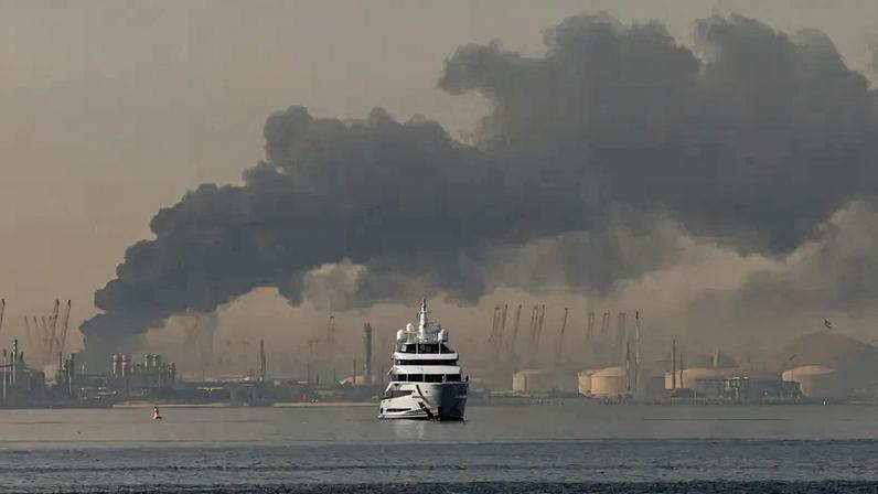 A yacht sails past a plume of smoke rising from the port of Jebel Ali following a reported Iranian strike in Dubai on March 1, 2026.