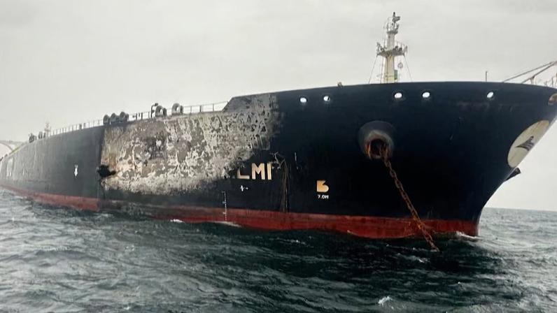Navio cargueiro de grande porte, com casco preto e sinais de desgaste e ferrugem, navegando em mar agitado sob céu nublado