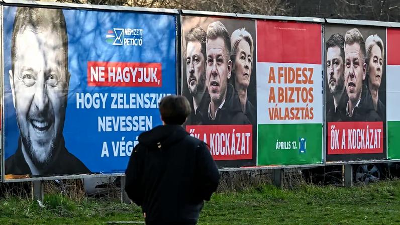 A pedestrian walks past billboards featuring Ukrainian President Volodymyr Zelensky, reading “Don’t let Zelensky have the last laugh,” and another billboard featuring Zelensky (left), Hungarian opposition leader Peter Magyar, and European Commission President Ursula von der Leyen, in Budapest.