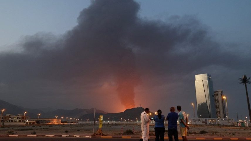 Trabalhadores estrangeiros observam uma coluna de fumaça preta após uma explosão na zona industrial de Fujairah, nos Emirados Árabes Unidos, em 3 de março de 2026. Foto de Fadel Senna/AFP