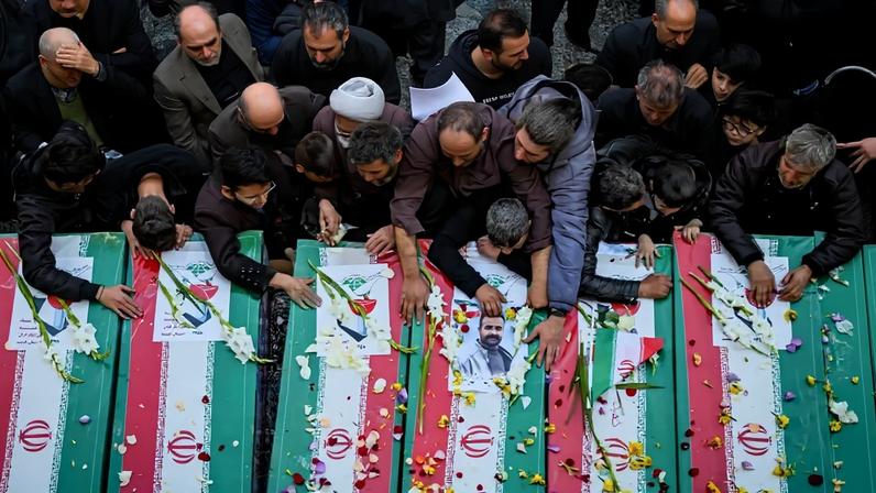 Mourners are seen from overhead as they lay flowers on caskets covered in Iranian flags at funeral in Qom.