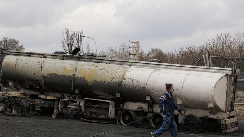 An Iranian civil defense member walks with a hose next to a destroyed fuel tanker following an overnight airstrike on the Shahran oil refinery in Tehran.