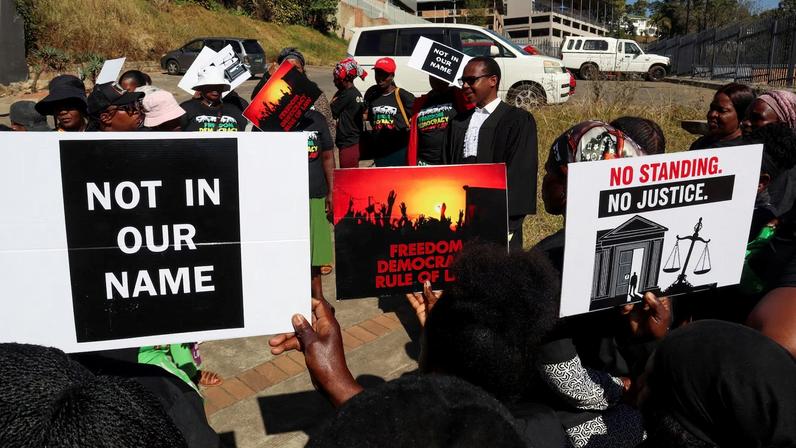 Protesters hold placards as a lawyer addresses them outside the court, after the hearing was postponed, in Mbabane, Eswatini, August 22, 2025. Activists are challenging a secretive agreement with former U.S. President Donald Trump's administration to accept third-country deportees, which they argue is unconstitutional.