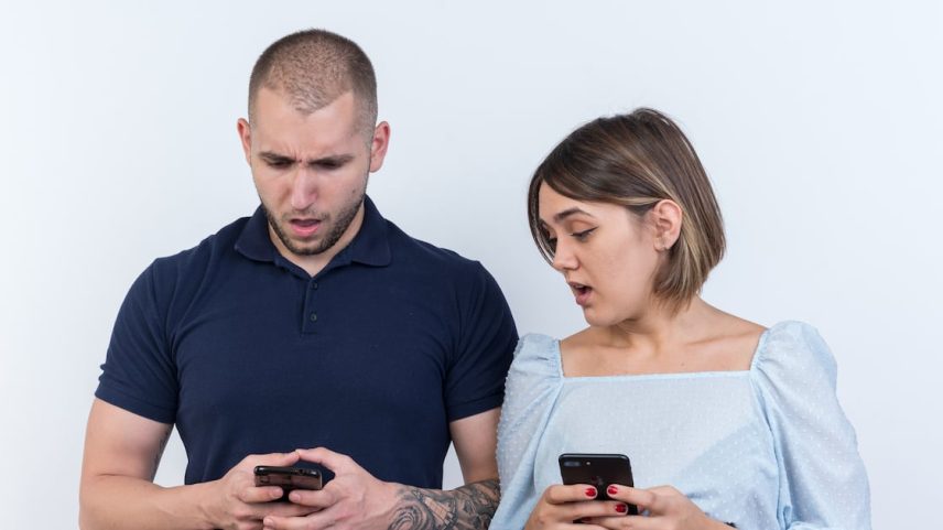 young beautiful couple man and woman holding smartphones looking confused and surprised standing over white background