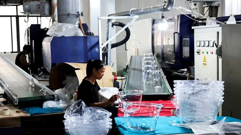 Funcionária removendo o excesso de plástico das peças de um produto de cozinha em uma fábrica na província de Zhejiang, na China, em 19 de maio de 2025.