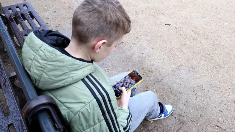 Menino mexe no celular sentado em banco