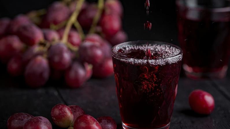 Um copo de suco de uva fresco, enlatamento de suco de uva. Fundo escuro, respingos e gotas no copo. Foto: Irina Sokolovskaya - stock.adobe.com/Adobe stock