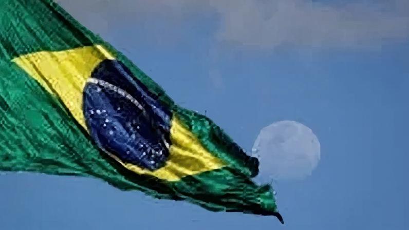 Bandeira do Brasil hasteada no mastro da Praça dos Três Poderes, tendo a lua ao fundo